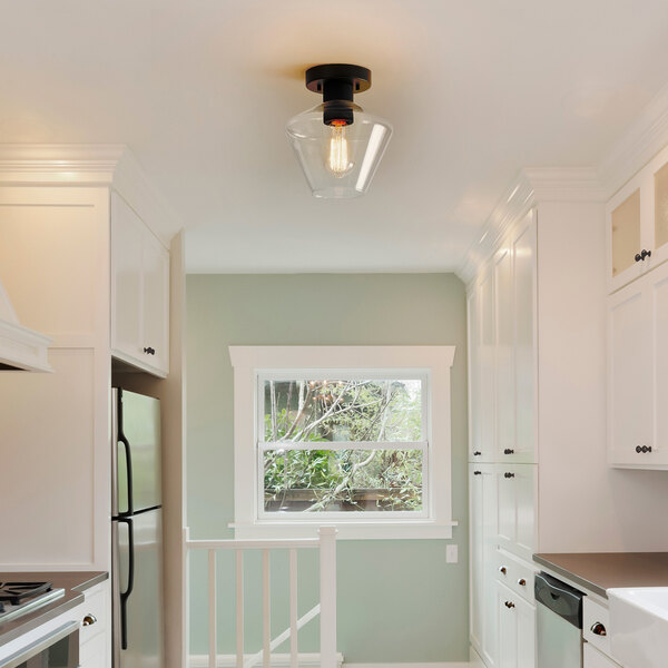 A matte black semi-flush mount ceiling light with a clear glass shade and a single exposed bulb.