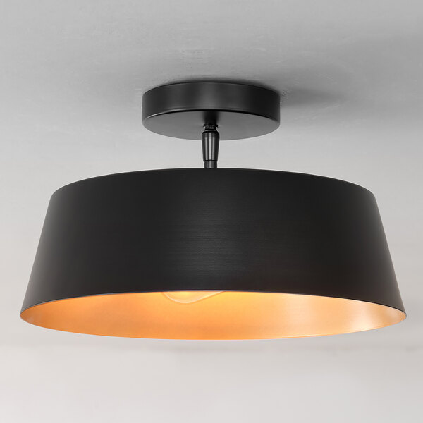A matte black flush mount ceiling light with a painted gold interior shade and two light bulbs.