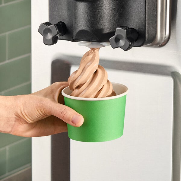 A hand holding a green cup of Turkey Hill chocolate soft serve ice cream.