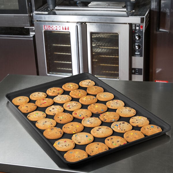 A black MFG fiberglass market display tray of cookies on a counter.