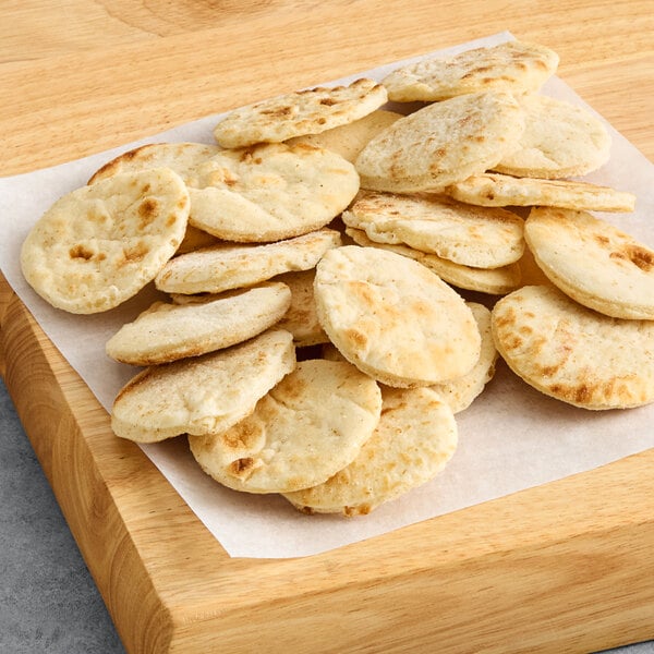 A pile of small, round, pre-grilled cocktail flatbreads on a piece of parchment paper.
