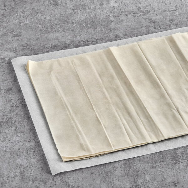 A Kontos fillo dough sheet on a table with a piece of food on a paper.