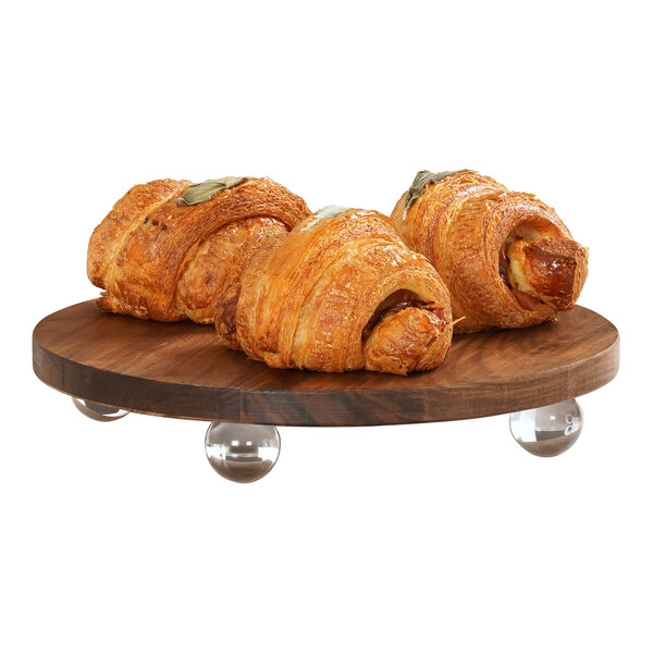 A group of croissants on a Cal-Mil walnut wood round display stand.