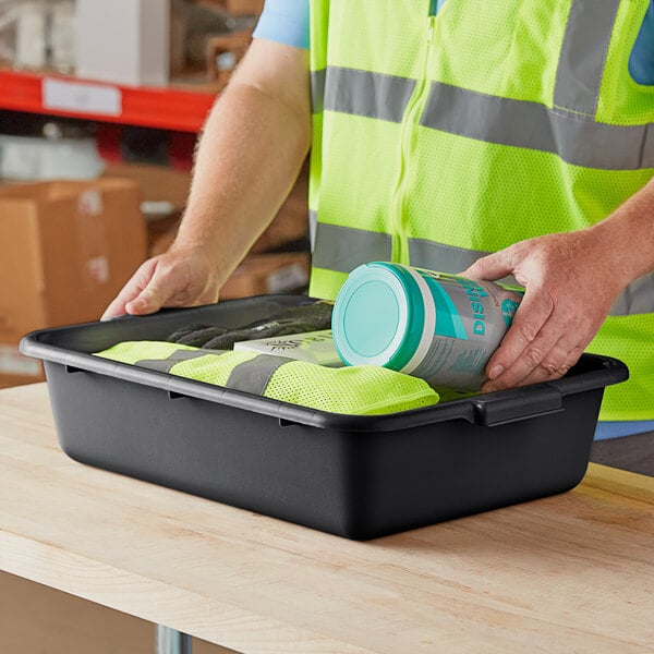 A black polypropylene utility bin containing various items, placed on a wooden table.