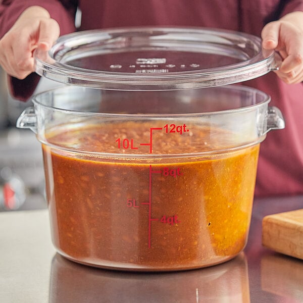 A clear 12-quart round polycarbonate food storage container with a lid, filled with a liquid food item.