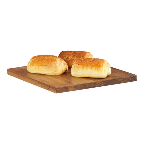 A group of bread rolls on a Cal-Mil walnut wood serving board on a table in a bakery display.
