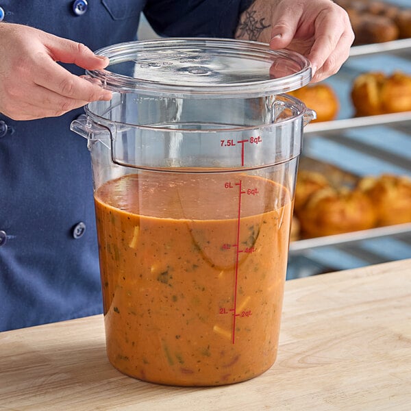 An 8-quart clear round polycarbonate food storage container with a lid, partially filled with soup or sauce.