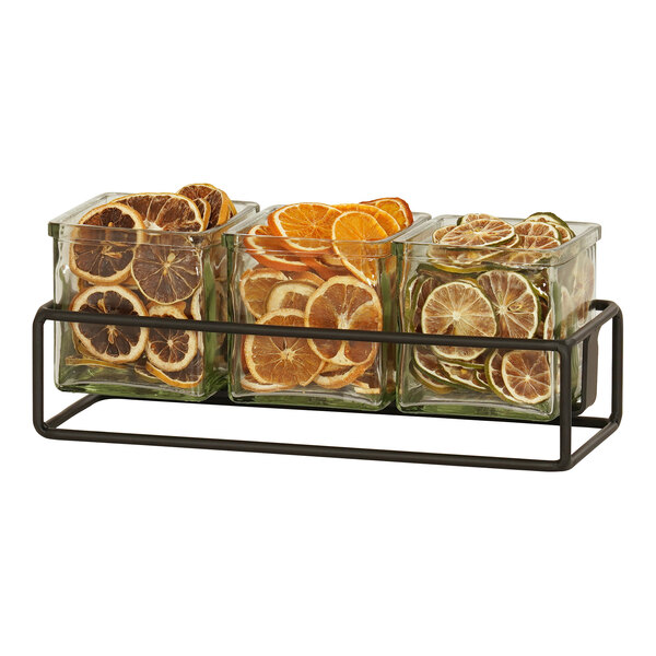 A black metal Cal-Mil condiment display holding three square glass containers with oranges and lemons.
