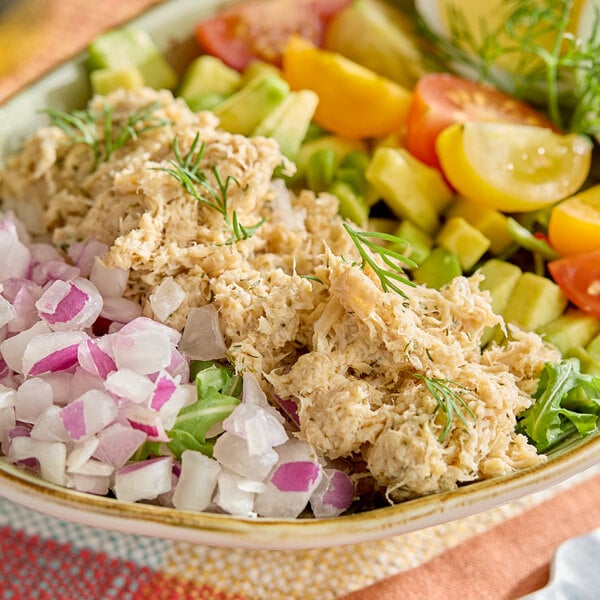 A bowl of plant-based vegan lemon and dill tuna served with chopped onions, tomatoes, cucumbers, and greens.