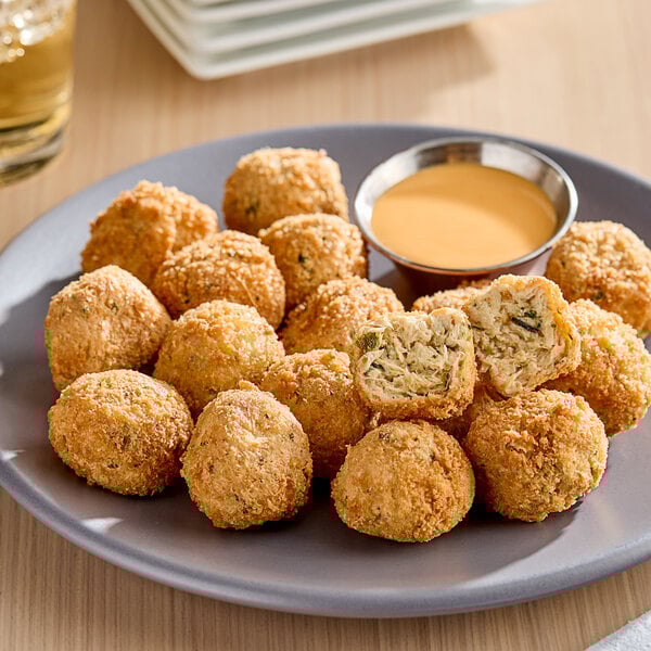 A plate of Jinka Plant-Based Vegan Crab Cake Poppers with a bowl of sauce.