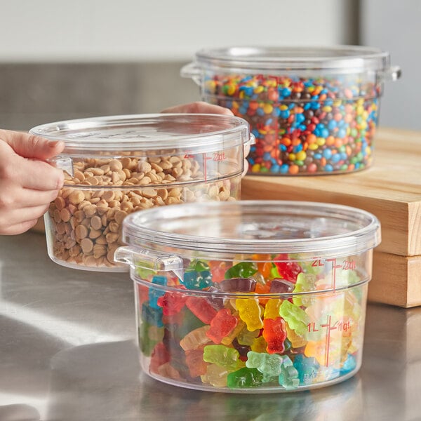 A clear round polycarbonate food storage container with a lid, filled with various candies and baking ingredients.