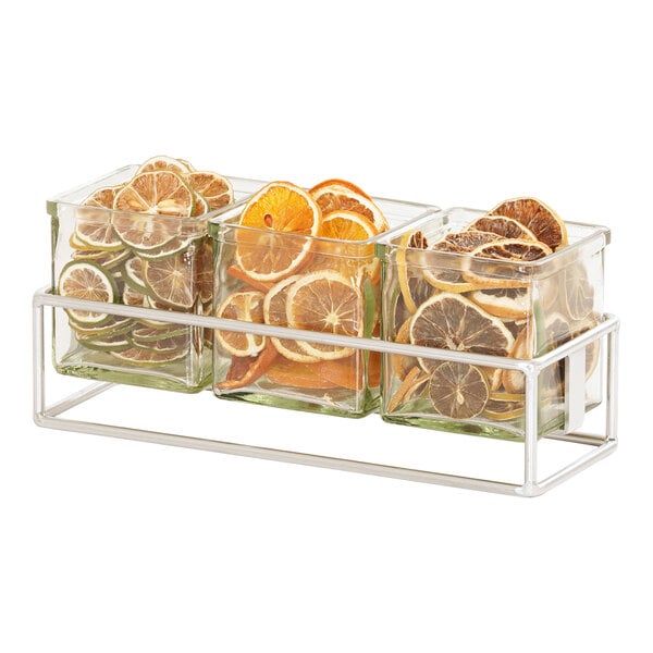 A Cal-Mil chrome condiment display with three square glass jars filled with citrus slices.