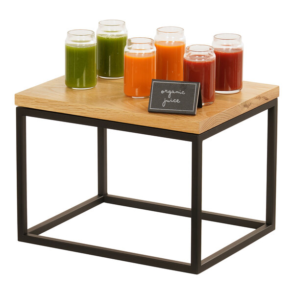 A black metal rectangular display riser on a table with glasses of juice on it.