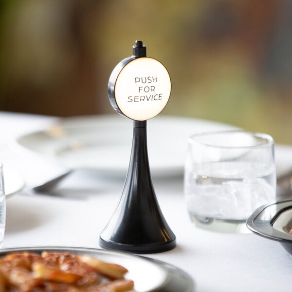 A black and white plastic "Push for Service" tabletop sign on a table with plates and glasses.