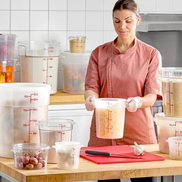 A translucent 12-quart round polypropylene food storage container with a lid, shown in a commercial kitchen setting.