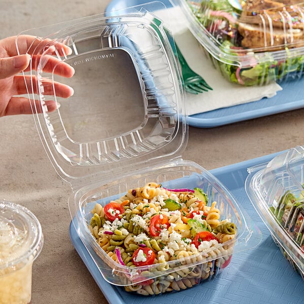 A hand holding a Choice clear plastic clamshell container of pasta and vegetables.
