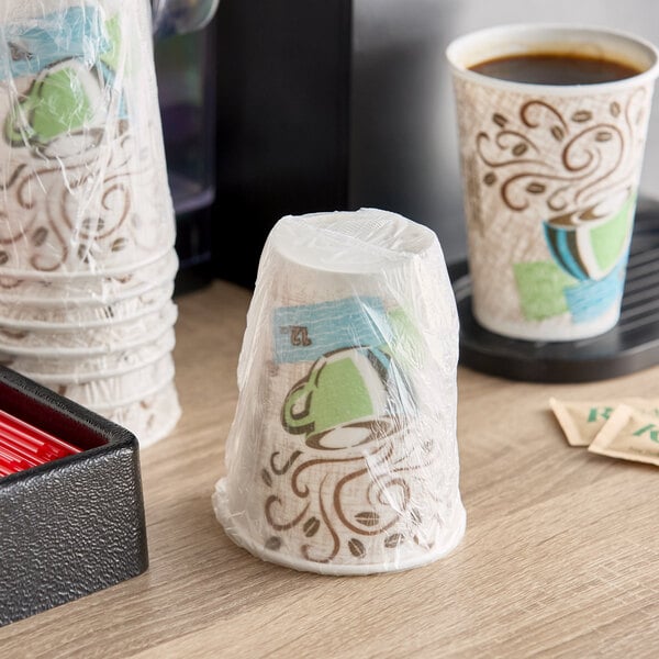 A stack of Dixie PerfecTouch paper hot cups in plastic bags on a counter with a container of coffee.