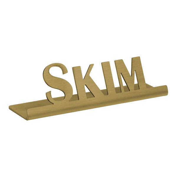 A vintage gold stainless steel tabletop sign with the word "skim" in polished brass.