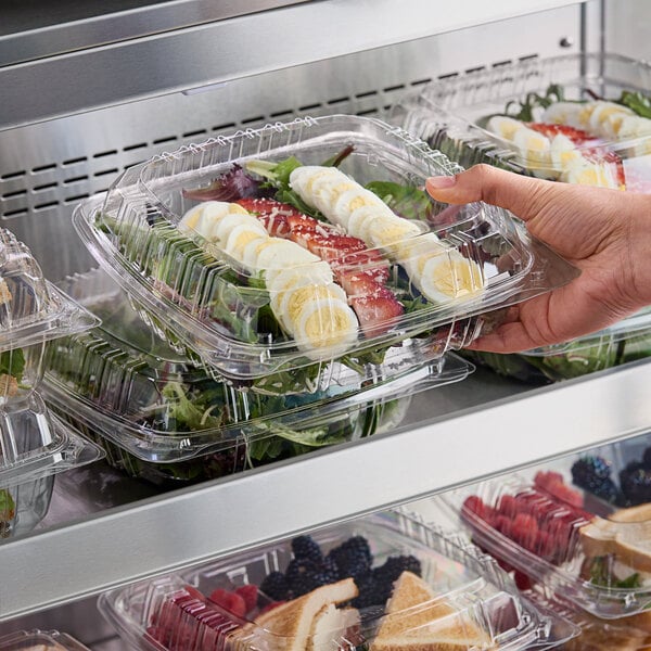 A hand holding a Choice clear plastic clamshell container of food.
