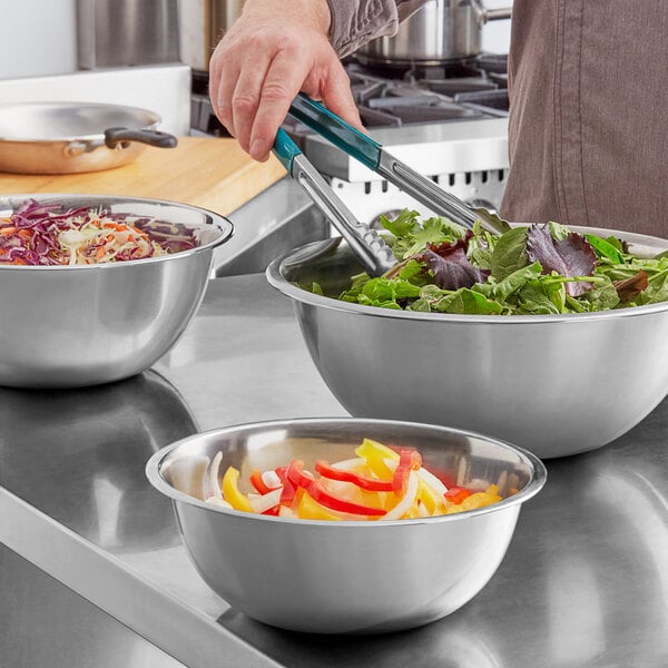 A set of three stainless steel mixing bowls filled with various vegetables on a kitchen counter.