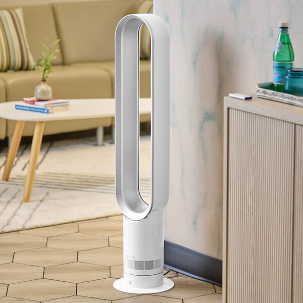 A white Dyson tower fan in a white room next to a couch.