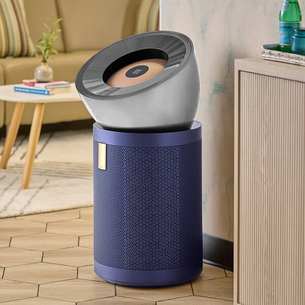 A nickel and blue Dyson air purifier on a wooden floor.