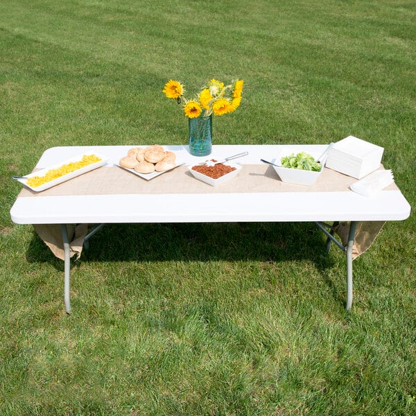A Lancaster Table & Seating white plastic folding table with food on it in an outdoor setup.