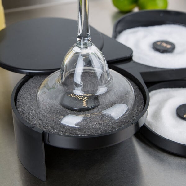 A wine glass sitting on a black tray with a glass of liquid and a black container of white salt with a clear lid.