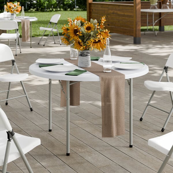A 48-inch round heavy-duty granite white plastic folding table with gray legs, set for dining and decorated with a vase of sunflowers.
