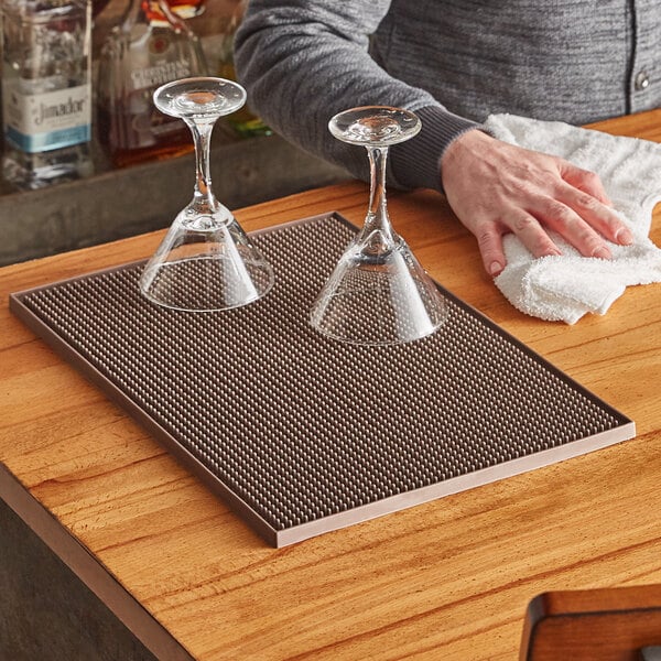 A man cleaning wine glasses on a wood bar mat.