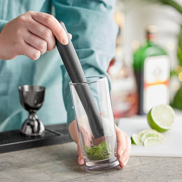 A person using a Choice black ribbed head muddler to make a drink.