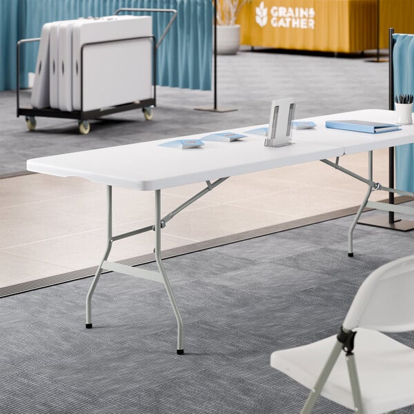 A 30 inch by 96 inch granite white plastic bi-folding table with gray legs.