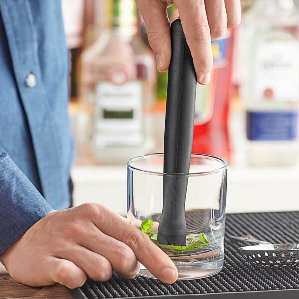 A hand holding a Choice black triangle-shaped muddler in a glass.