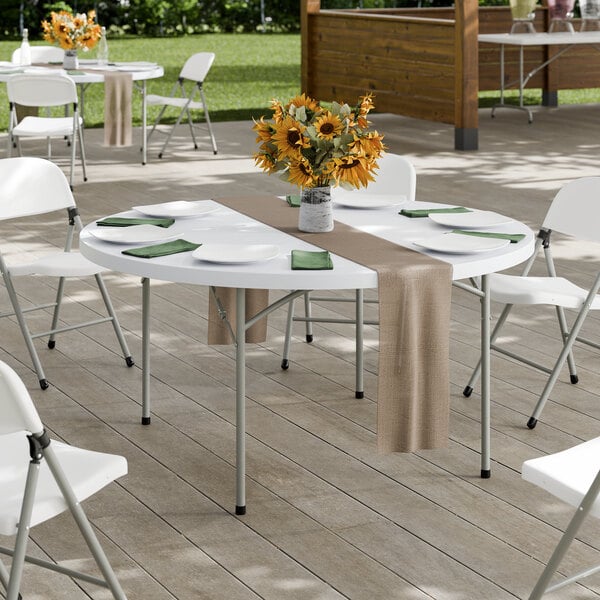 A 60-inch round heavy-duty granite white plastic folding table with gray legs, set outdoors with chairs and table settings.