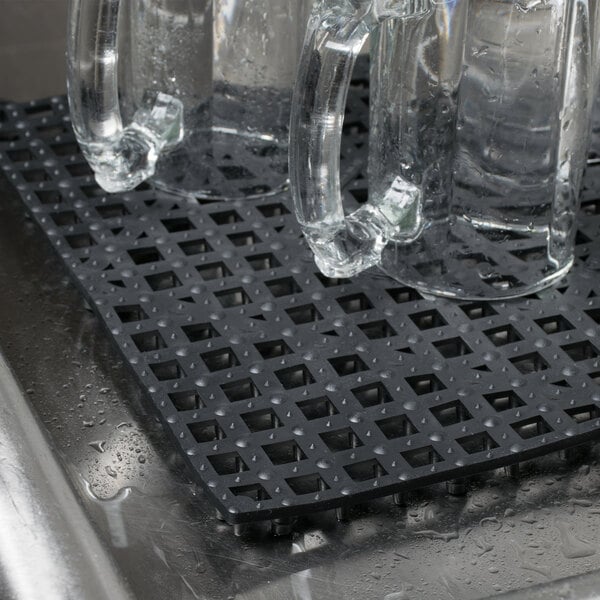 A pair of clear glass mugs on a black interlocking bar mat.