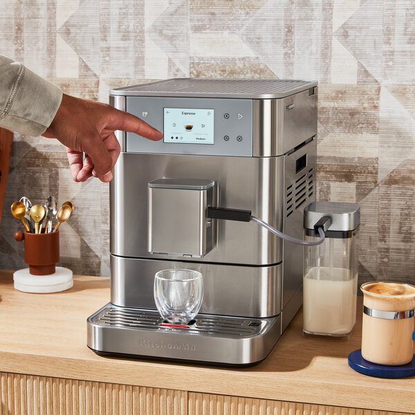 A person using the touch screen on a KitchenAid stainless steel espresso machine.