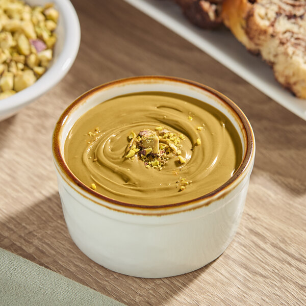 A Vor Pistachio Cream pail on a table with bread and nuts.