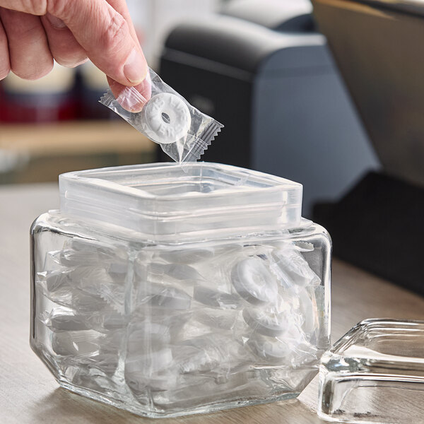 A hand putting LIFE SAVERS Pep-O-Mint Hard Candy into a clear container.