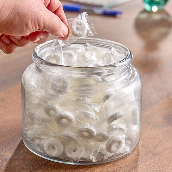 A hand putting a bag of LIFE SAVERS Wint-O-Green Hard Candy into a jar.