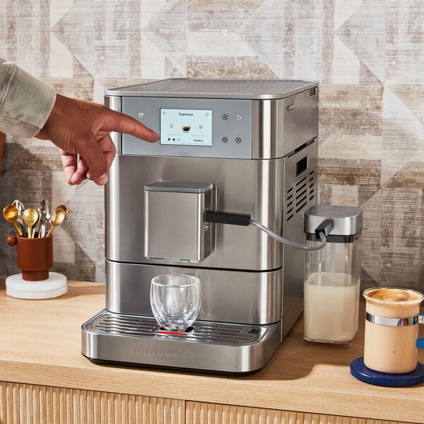 A person using a KitchenAid stainless steel espresso machine to press a button to make a drink.