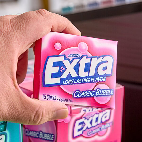 A hand holding a pink box of Wrigley's EXTRA bubble gum.