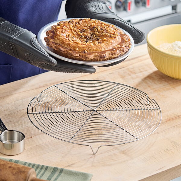 A round, footed stainless steel cooling rack on a wooden countertop.