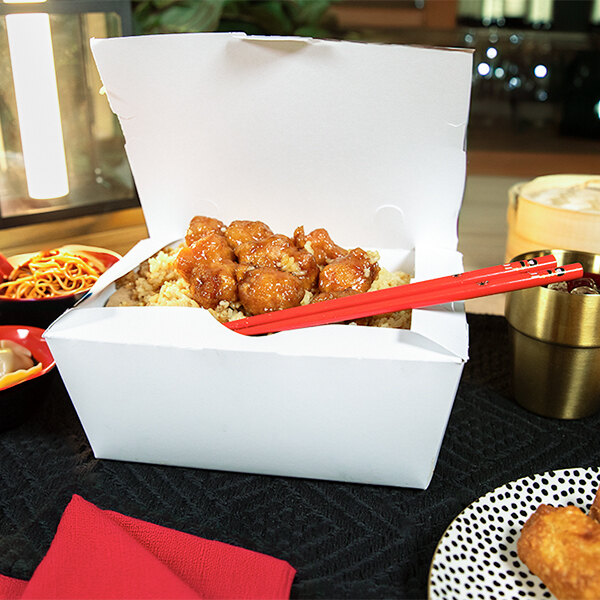 A white take-out box filled with food and chopsticks.