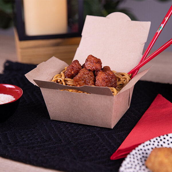 A Southern Champion kraft paper take-out container filled with noodles and meatballs on a table with chopsticks.