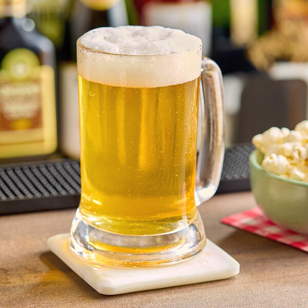 A glass of beer with foam on a coaster next to a bowl of popcorn.