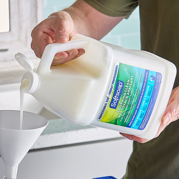 A person pouring a jug of Softsoap liquid hand soap into a sink.