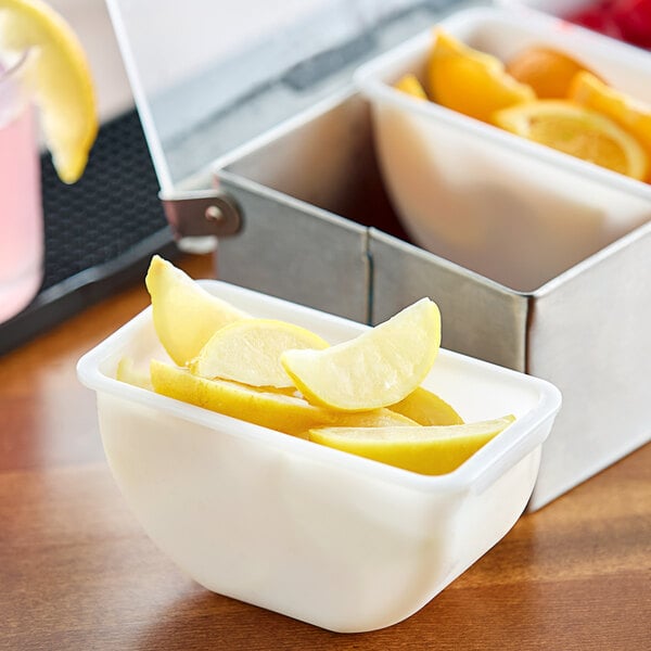 A white container of Dole lemon wedges on a table with bowls of lemons and oranges.