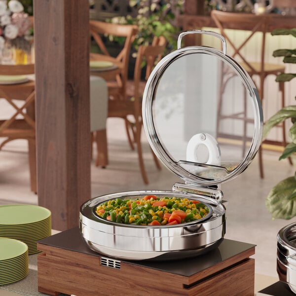 An Acopa stainless steel chafer with a glass lid on a table with food inside.