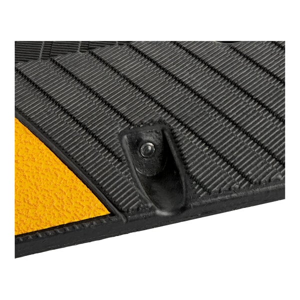 A close-up of a black and yellow rubber speed bump with a textured surface and a mounting hole.