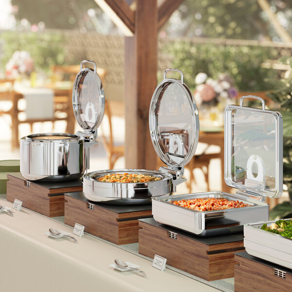 A buffet with food on a table with an Acopa Manchester stainless steel soup chafer with a glass top.